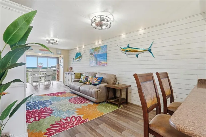 Open living area featuring wood-finish flooring, white shiplap accent wall, and recessed lighting - Virtually Edited Image