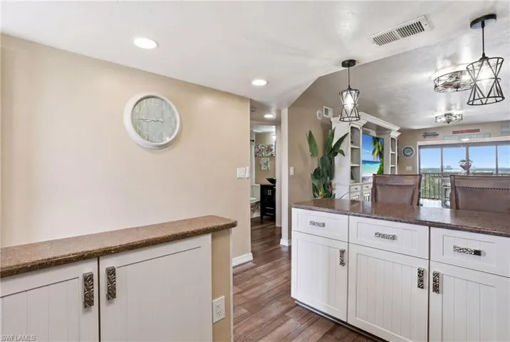 Kitchen island with a granite-style countertop, white cabinetry with decorative hardware, and wood-finish flooring - Virtually Edited Image