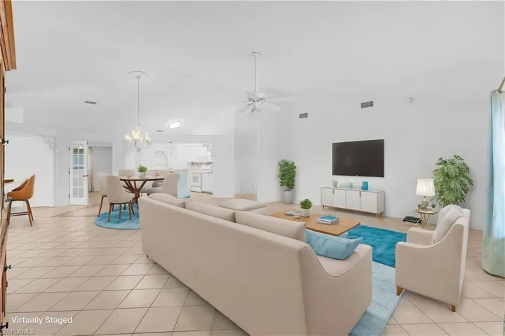 Living room featuring vaulted ceiling, light tile patterned flooring, a ceiling fan, and a chandelier virtually staged