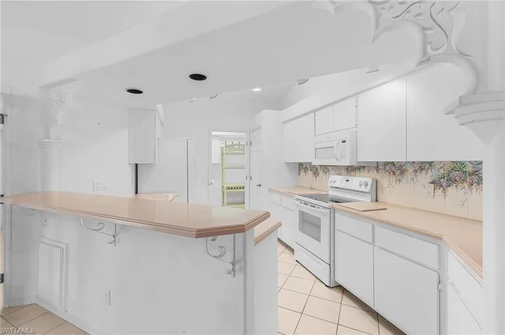 Kitchen featuring white cabinets, white appliances, a breakfast bar area, light countertops, and a peninsula
