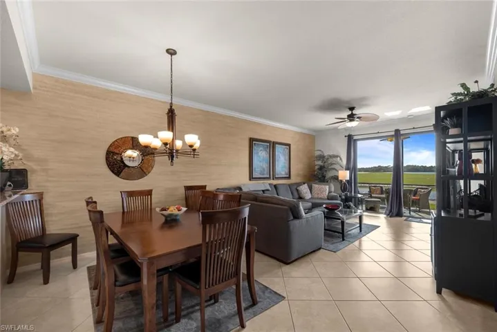 Tiled dining room with ceiling fan with notable chandelier and crown molding