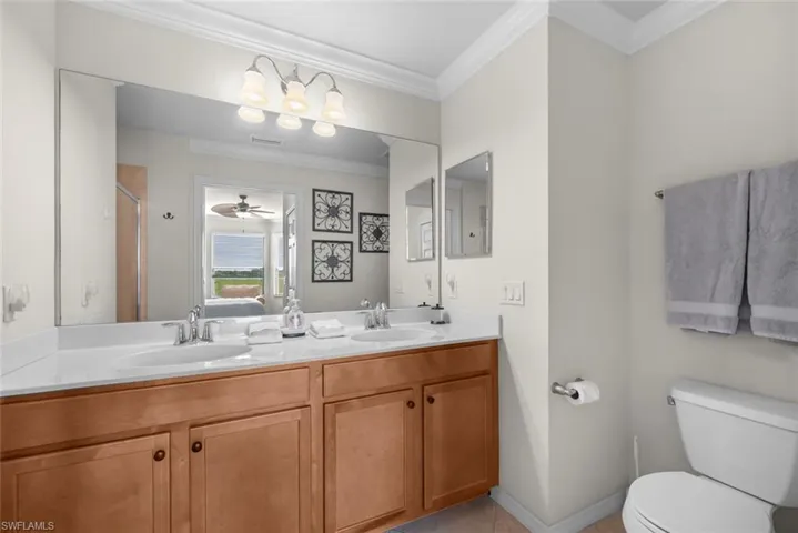 Bathroom featuring tile patterned flooring, toilet, vanity, ceiling fan, and ornamental molding
