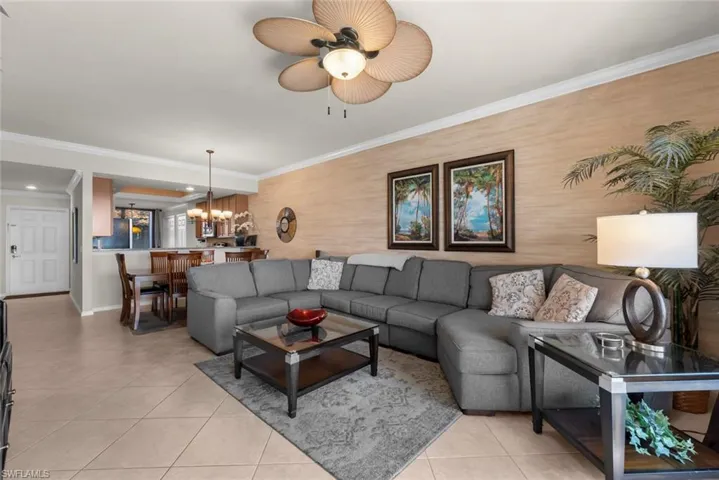 Tiled living room featuring ceiling fan with notable chandelier and ornamental molding