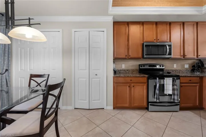 Kitchen featuring dark stone counters, appliances with stainless steel finishes, light tile patterned flooring, and crown molding