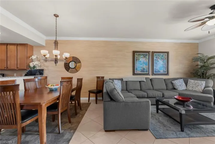 Tiled living room featuring ceiling fan with notable chandelier and crown molding