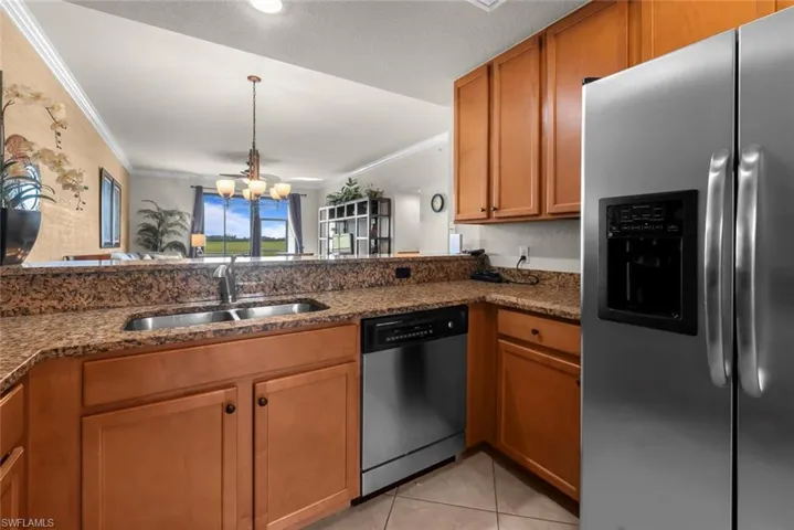 Kitchen with dark stone counters, appliances with stainless steel finishes, a notable chandelier, and sink