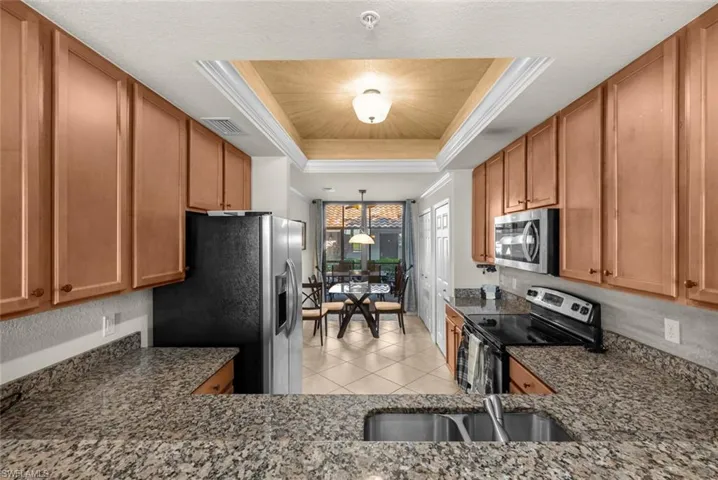 Kitchen with a raised ceiling, appliances with stainless steel finishes, light tile patterned floors, ornamental molding, and sink