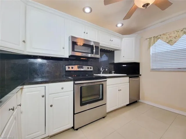 Kitchen featuring decorative backsplash, appliances with stainless steel finishes, white cabinets, crown molding, and light tile patterned floors
