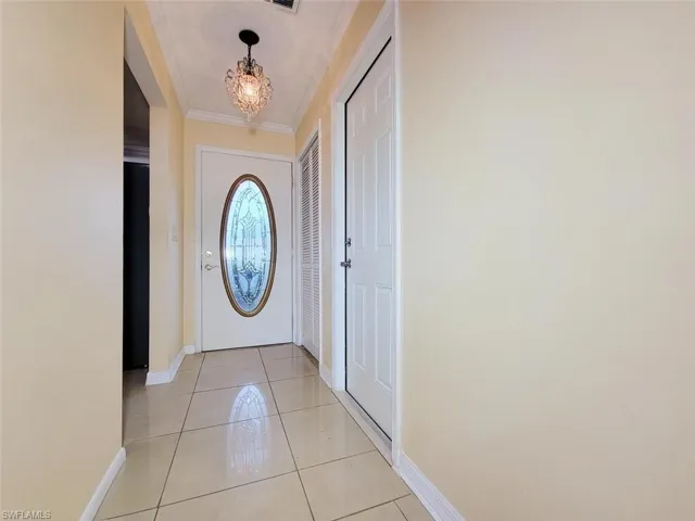 Doorway to outside featuring tile patterned floors, a chandelier, and crown molding