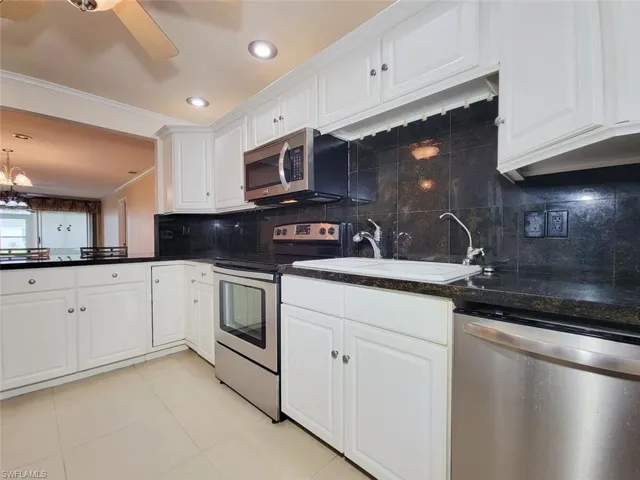 Kitchen featuring backsplash, appliances with stainless steel finishes, ornamental molding, white cabinetry, and light tile patterned flooring