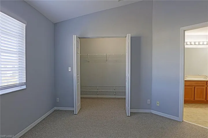 Unfurnished bedroom with light colored carpet, lofted ceiling, a closet, and ensuite bath