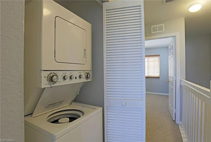 Laundry area with light colored carpet, stacked washer and dryer, and a textured ceiling