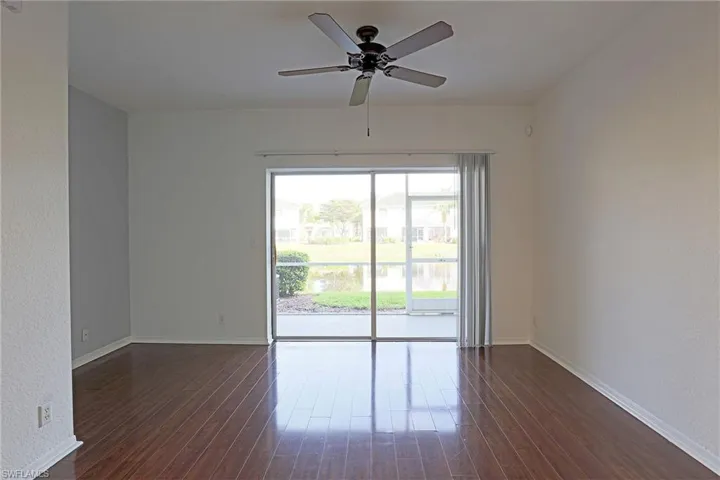 Empty room featuring a ceiling fan, a textured wall, dark wood finished floors, and a water view