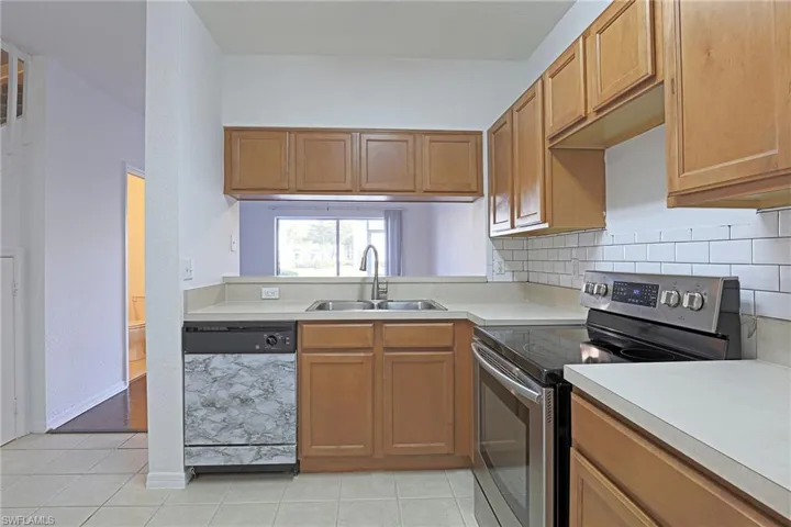 Kitchen with electric range, dishwashing machine, light countertops, wood finish cabinets, and light tile patterned floors