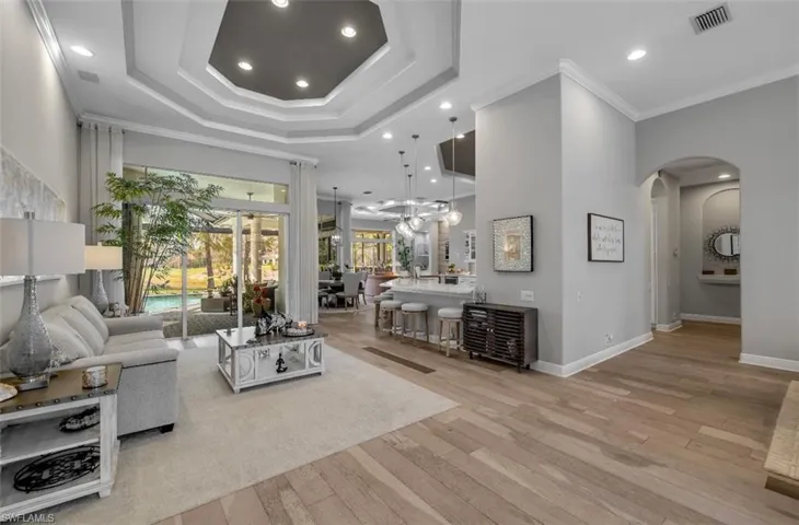 Living area featuring crown molding, recessed lighting, light wood finished floors, arched walkways, and a high ceiling
