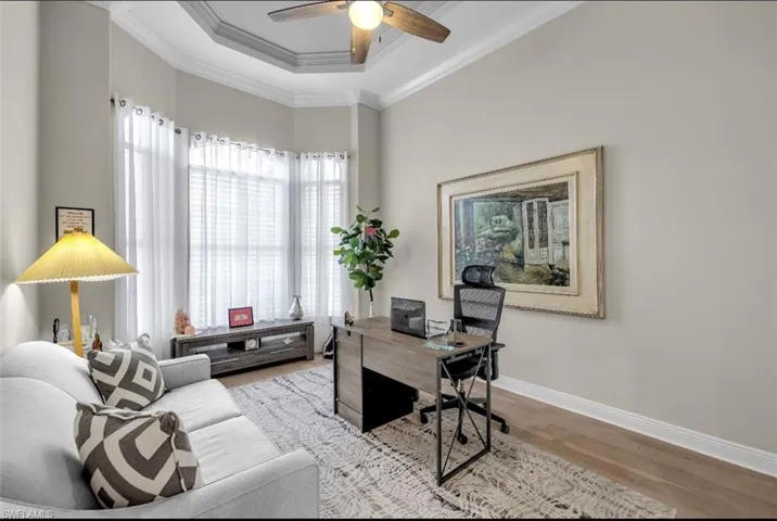 Office space with ornamental molding, a raised ceiling, ceiling fan, and light wood-type flooring