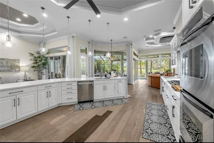 Kitchen with open floor plan, appliances with stainless steel finishes, white cabinets, ornamental molding, and decorative light fixtures