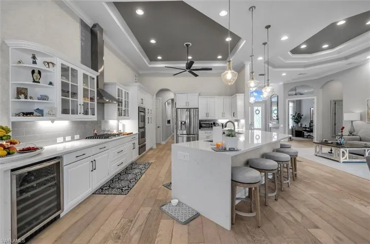Kitchen featuring arched walkways, beverage cooler, white cabinets, hanging light fixtures, and crown molding