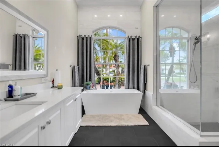 Bathroom with a shower stall, a freestanding tub, vanity, dark tile patterned flooring, and healthy amount of natural light