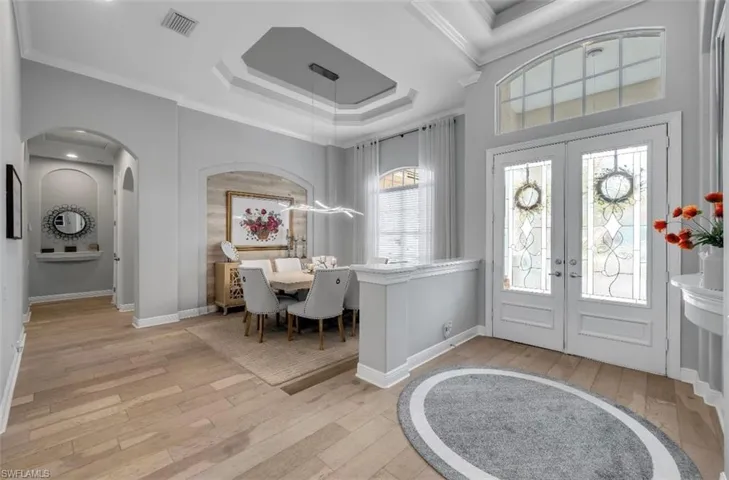 Entryway with french doors, ornamental molding, light wood finished floors, a tray ceiling, and arched walkways
