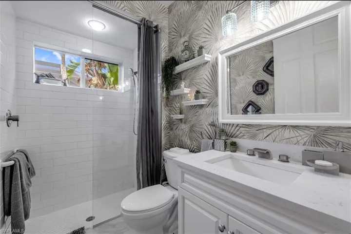 Bathroom featuring wallpapered walls, tiled shower, and vanity