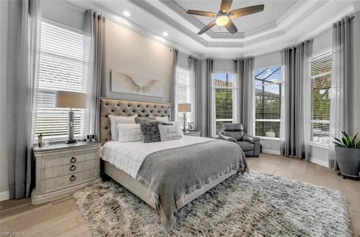 Bedroom featuring light wood-style flooring, a raised ceiling, crown molding, and ceiling fan