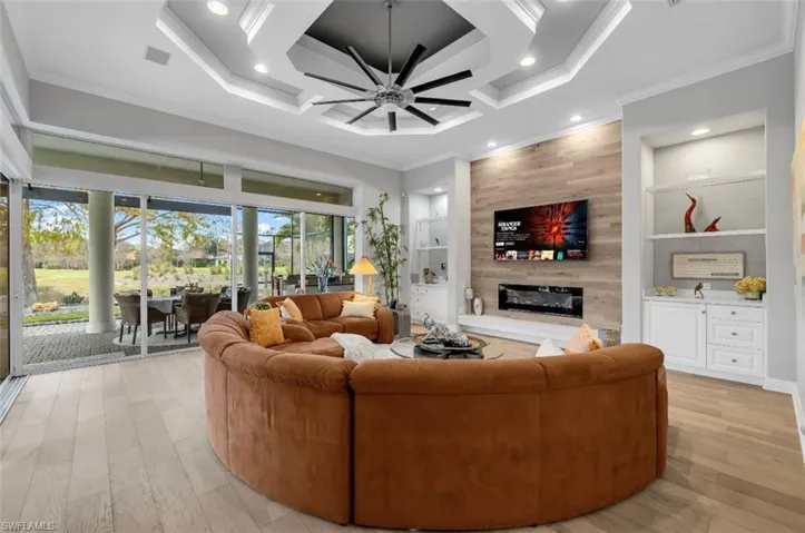 Living room with built in shelves, a large fireplace, a ceiling fan, recessed lighting, and coffered ceiling