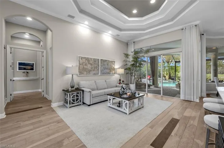 Living room featuring ornamental molding, light wood-style flooring, recessed lighting, a towering ceiling, and arched walkways