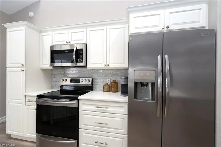 Kitchen featuring dark hardwood / wood-style floors, appliances with stainless steel finishes, white cabinets, and tasteful backsplash