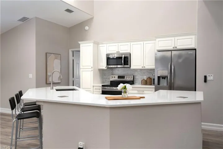 Kitchen with white cabinetry, stainless steel appliances, tasteful backsplash, a spacious island, and sink