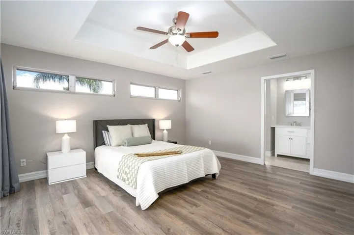 Bedroom with a raised ceiling, ceiling fan, ensuite bathroom, and multiple windows