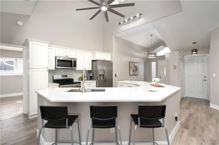 Kitchen featuring stainless steel appliances, a large island with sink, white cabinetry, and decorative light fixtures