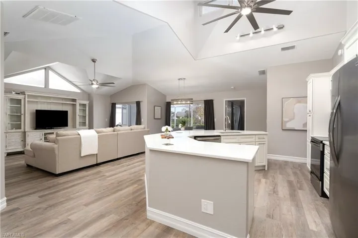 Kitchen with white cabinets, lofted ceiling, light hardwood / wood-style flooring, stainless steel appliances, and a center island with sink