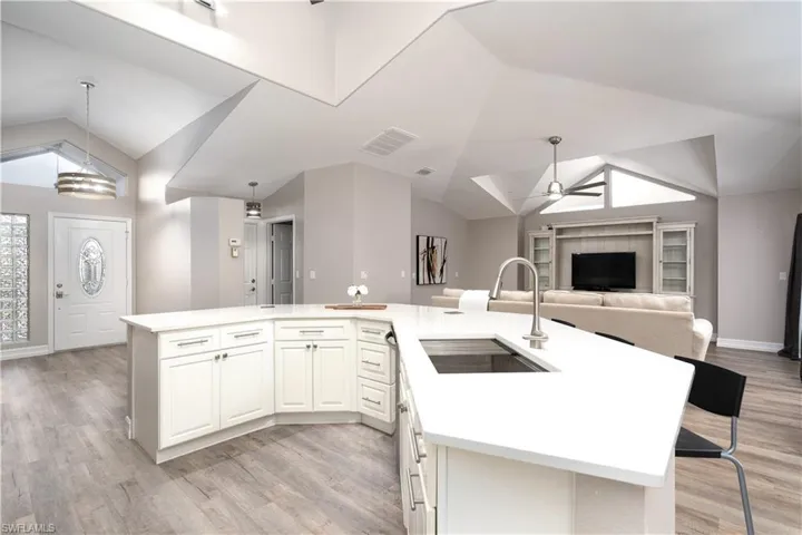 Kitchen featuring lofted ceiling, decorative light fixtures, sink, a kitchen island with sink, and ceiling fan with notable chandelier