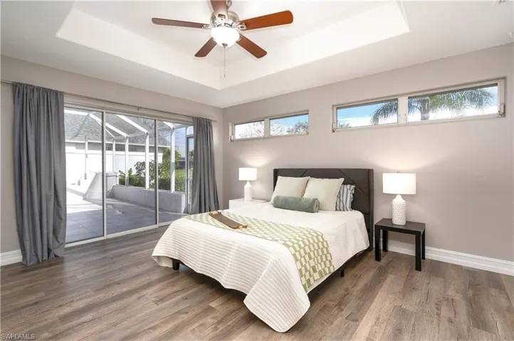 Bedroom with ceiling fan, access to exterior, dark hardwood / wood-style flooring, and a tray ceiling