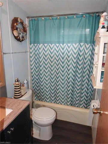 Full bathroom with a textured ceiling, shower / bath combo, hardwood / wood-style floors, toilet, and vanity