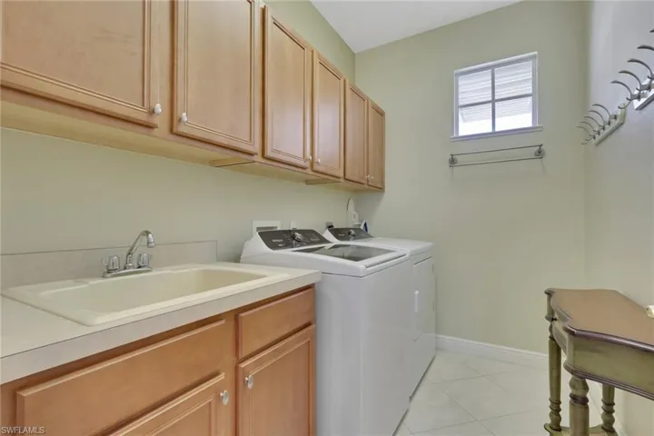 Laundry area with light tile patterned floors, washer and dryer, and cabinet space