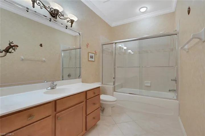 Full bathroom featuring crown molding, vanity, light tile patterned floors, and enclosed tub / shower combo