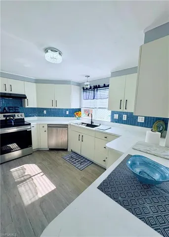 Kitchen featuring appliances with stainless steel finishes, tasteful backsplash, light wood finished floors, and under cabinet range hood