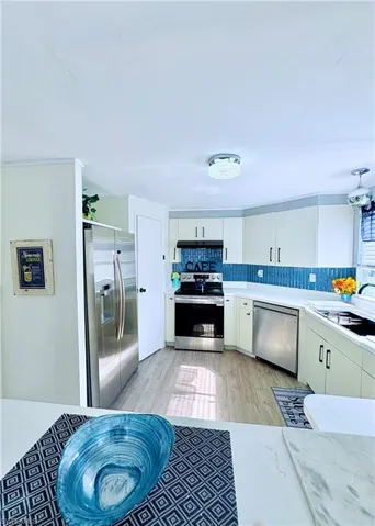 Kitchen with appliances with stainless steel finishes, white cabinetry, tasteful backsplash, light wood-style floors, and light stone counters