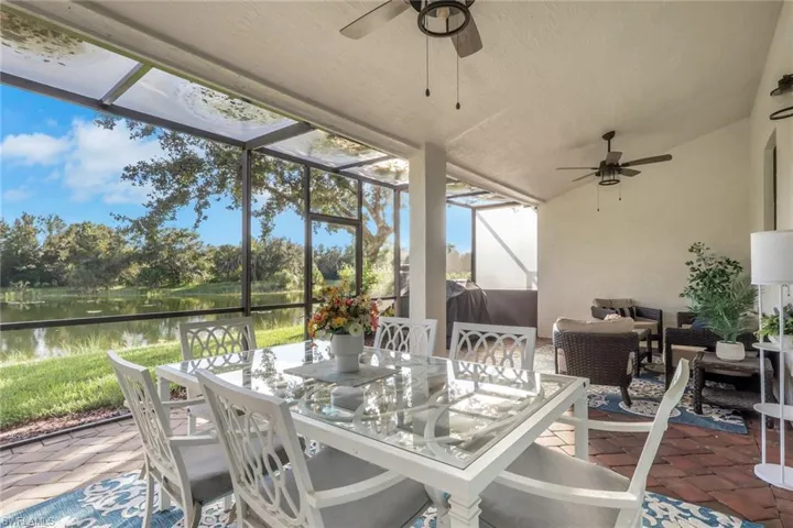 Screened-in lanai featuring terra cotta paver flooring, overhead ceiling fans, and a metal-framed enclosure overlooking a pond