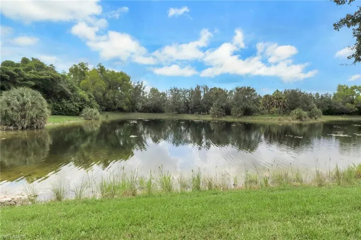 Waterfront lot featuring a natural pond, manicured lawn, and mature perimeter trees