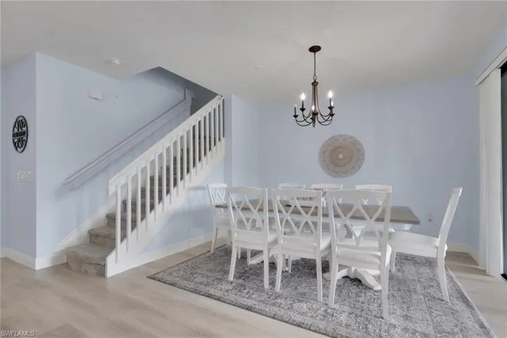 Open-concept room featuring wood-finish flooring, a classic multi-arm chandelier, and a staircase with a white balustrade