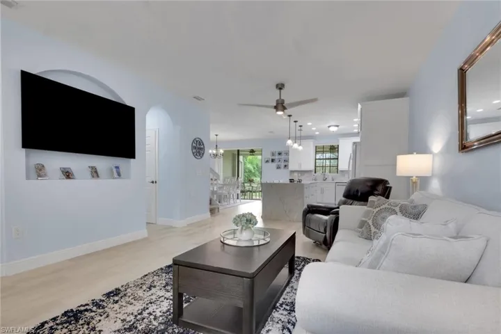 Open-concept living space featuring wood-finish flooring, an arched wall niche with integrated shelving, a central island with stone-finish countertop, and recessed ceiling lighting