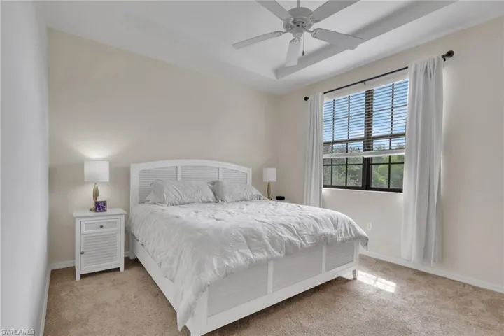 Bedroom featuring a tray ceiling, ceiling fan with light kit, and large windows with integrated grids