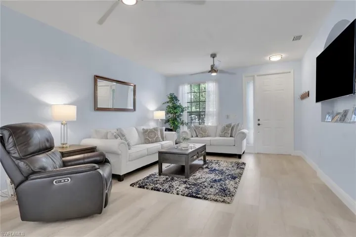 Living area featuring light-toned wood-finish flooring, recessed wall niche, multi-panel entry door with sidelight, and ceiling-mounted fans