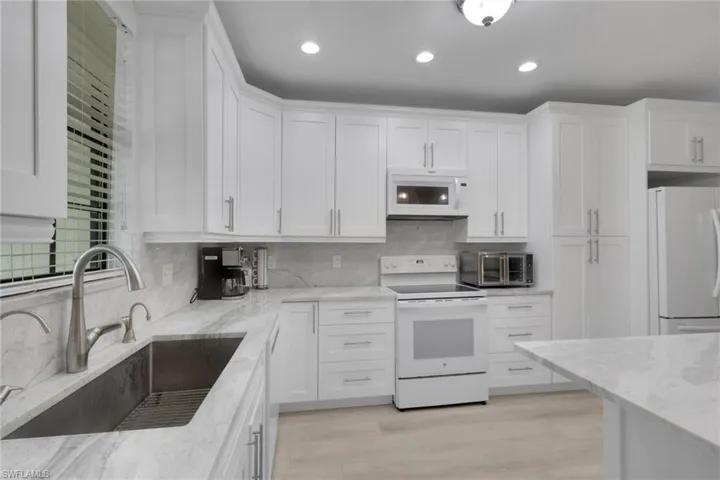 Kitchen featuring white shaker-style cabinetry, stone-finish countertops, stainless steel undermount sink, recessed lighting, and wood-finish flooring