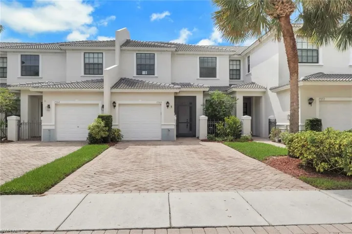 Two-story exterior featuring a light-toned stucco facade, shingle roof, paved herringbone driveway, and integrated garage doors