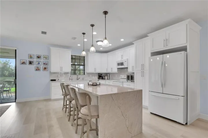 Kitchen featuring white shaker-style cabinetry, expansive stone-finish center island, light-toned wood-finish flooring, and a suite of white appliances