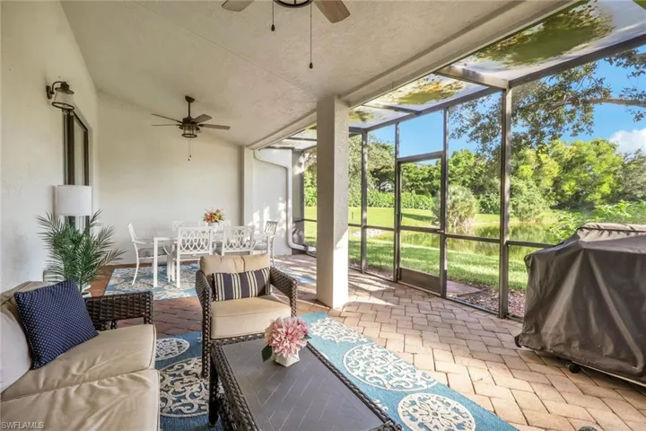 Screened-in patio featuring brick-paver flooring, multiple ceiling fans, and wall-mounted light fixtures, overlooking a pond